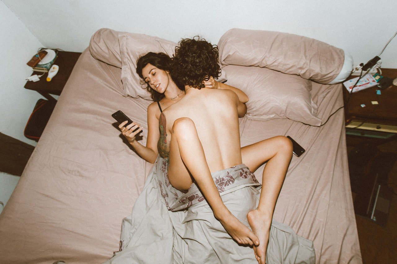 Un couple au lit, la femme semble désintéressée des caresses de l’homme.