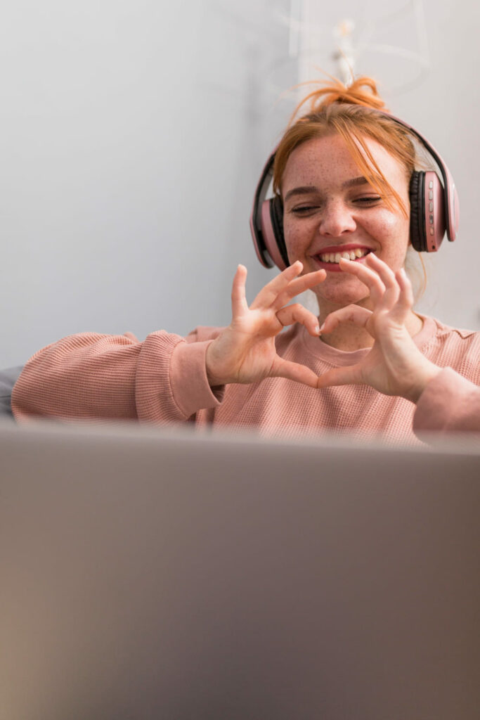 Une jeune femme heureuse qui fait un coeur avec ses mains pour son partenaire de relation à distance lors d'un appel vidéo