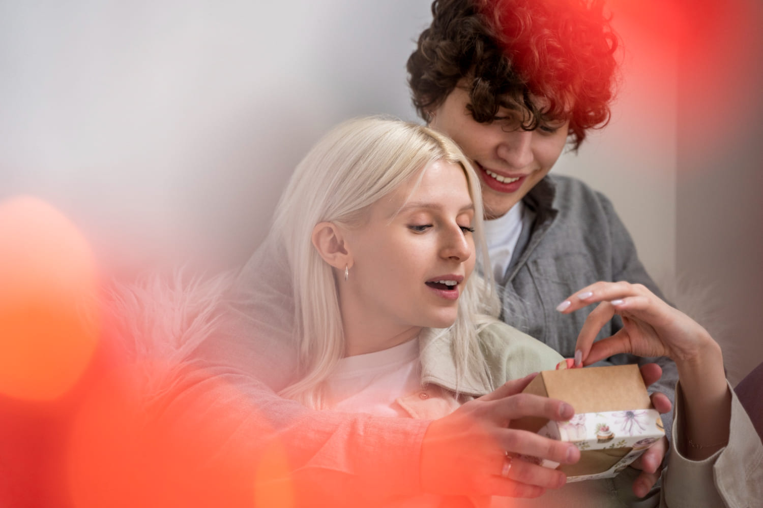Faire une surprise Ă  son amoureux sans argent Couple souriant sâenlaçant dans un salon et qui ouvre un cadeau